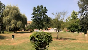 A park with a well-maintained lawn, a variety of trees, and a small building in the background. - Gîte Le Lavoir - Domaine l'Étang des Mirandes with Shared Pool (Varaignes)