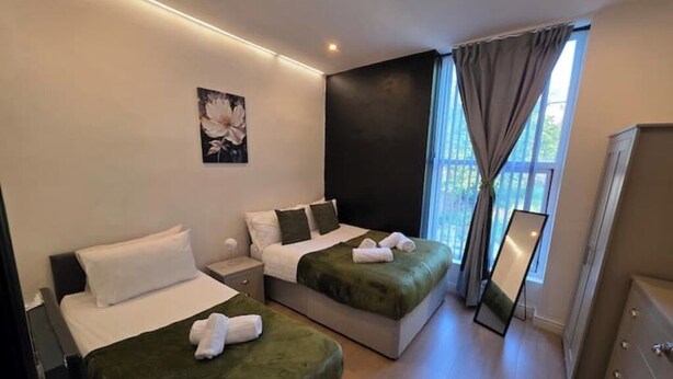 A hotel room with two beds, a large window with curtains, a mirror, and a dresser.