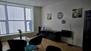 A living room with a dining area, a large window, a flat-screen TV, and artwork on the walls.
