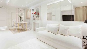 A modern living room with a white sofa, a dining table with chairs, a fireplace, and a large mirror. - La Perle - T2 with terrace, air conditioning & parking near Toulouse city center (Toulouse)