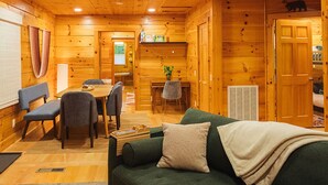 Un intérieur de chalet chaleureux avec un canapé vert, des murs en bois, un coin repas et une cuisine.
