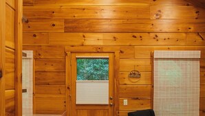 L’intérieur d’un chalet en bois comprend une table à manger, des chaises, un canapé, une fenêtre donnant sur les arbres et une porte.