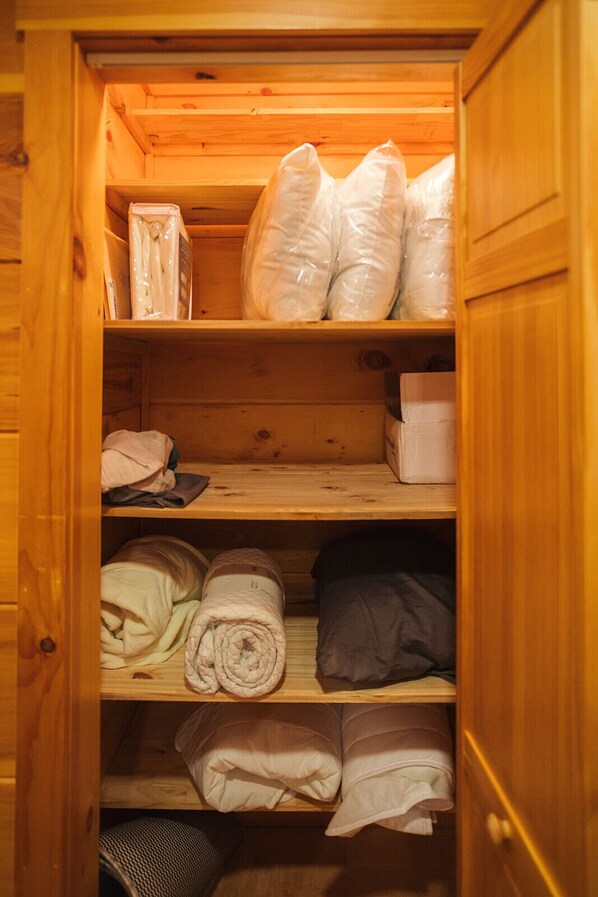 A wooden cabinet with shelves containing folded blankets, pillows, and a box.