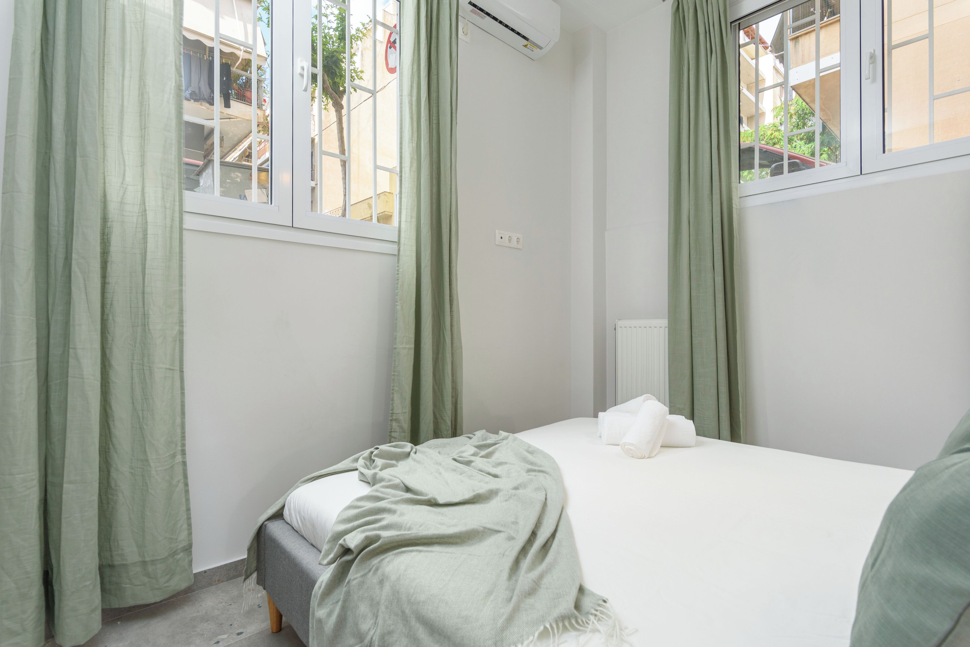 Un dormitorio con cama, cortinas verdes y un equipo de aire acondicionado.