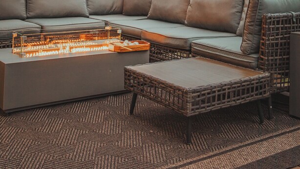 A wooden pergola with string lights, a sectional sofa, and a fire feature.