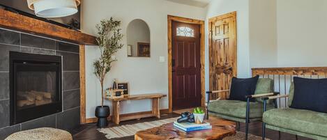 Ein gemütliches Wohnzimmer mit Kamin, grünem Sofa, Couchtisch aus Holz und einer Bank.