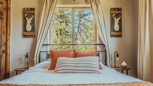 A bed with a patterned pillow, a bedside lamp, and a view of trees through a window.
