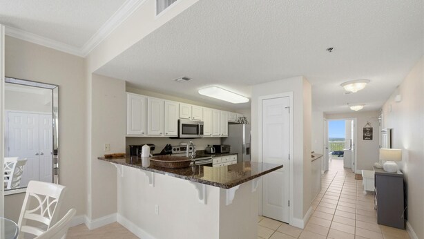 A kitchen with white cabinets, a microwave, and a refrigerator. There is a dining area with a table and chairs. - Palacio 1506 (Pensacola)