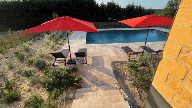A backyard with a swimming pool, two lounge chairs, and red umbrellas.