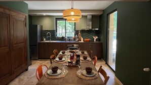 A modern kitchen with dark green walls, a wooden dining table set for four, and a large window providing natural light.