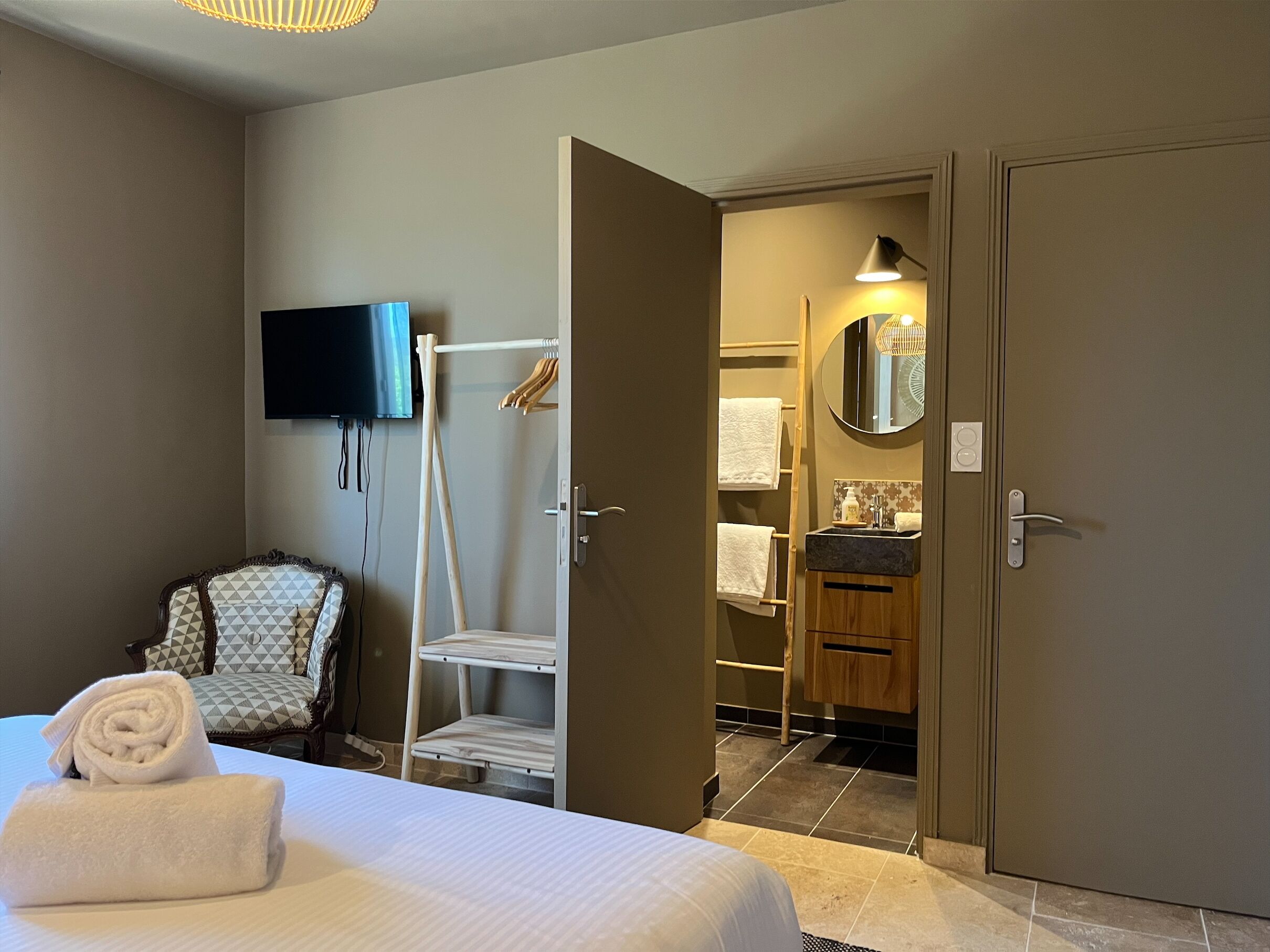 Een hotelkamer met een bed, een stoel, een televisie, een kledingkast en een badkamer die door een open deur zichtbaar is.