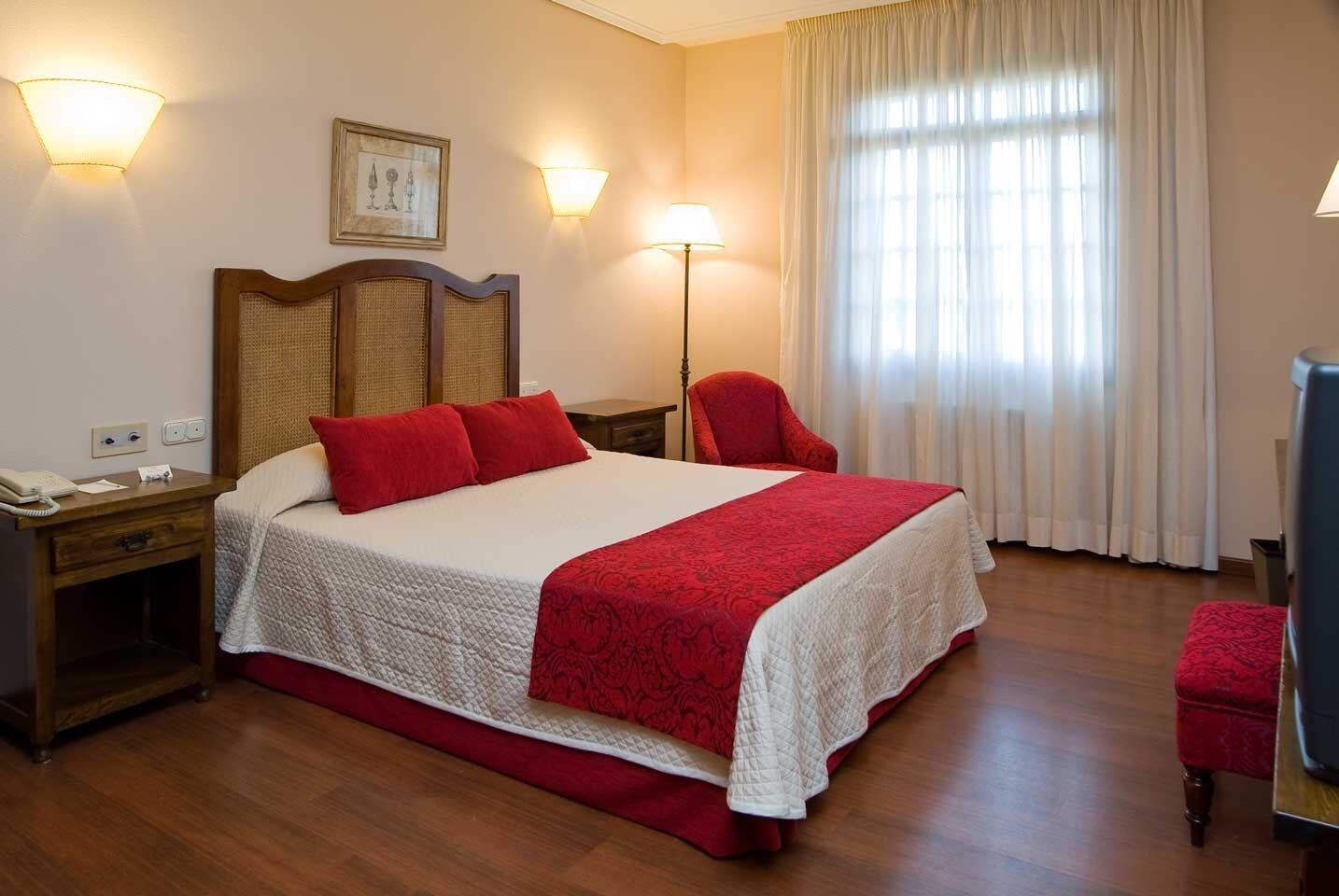 Habitación de hotel con una cama grande, dos mesitas de noche, una silla, un escritorio, una lámpara y un cuadro en la pared.