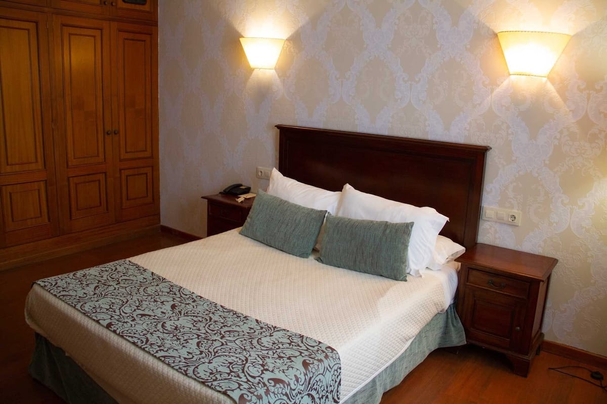A neatly made bed with a patterned bedspread, two bedside lamps, and a wooden nightstand with a telephone.