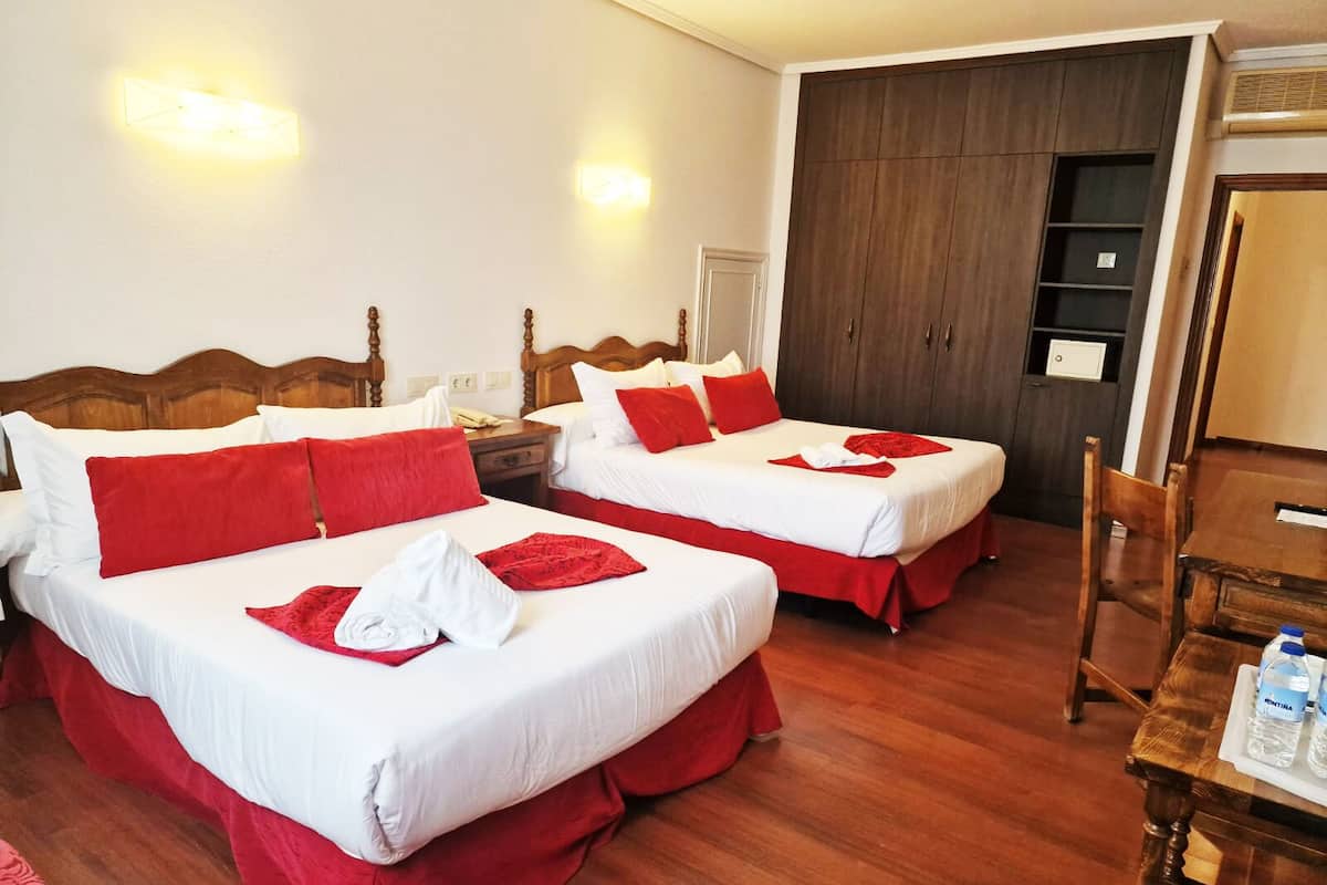 A hotel room with two beds, each with red and white bedding, a wooden headboard, a wooden table with water bottles, and a wardrobe.