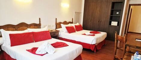 A hotel room with two beds, each with red and white bedding, a wooden headboard, a wooden table with water bottles, and a wardrobe.