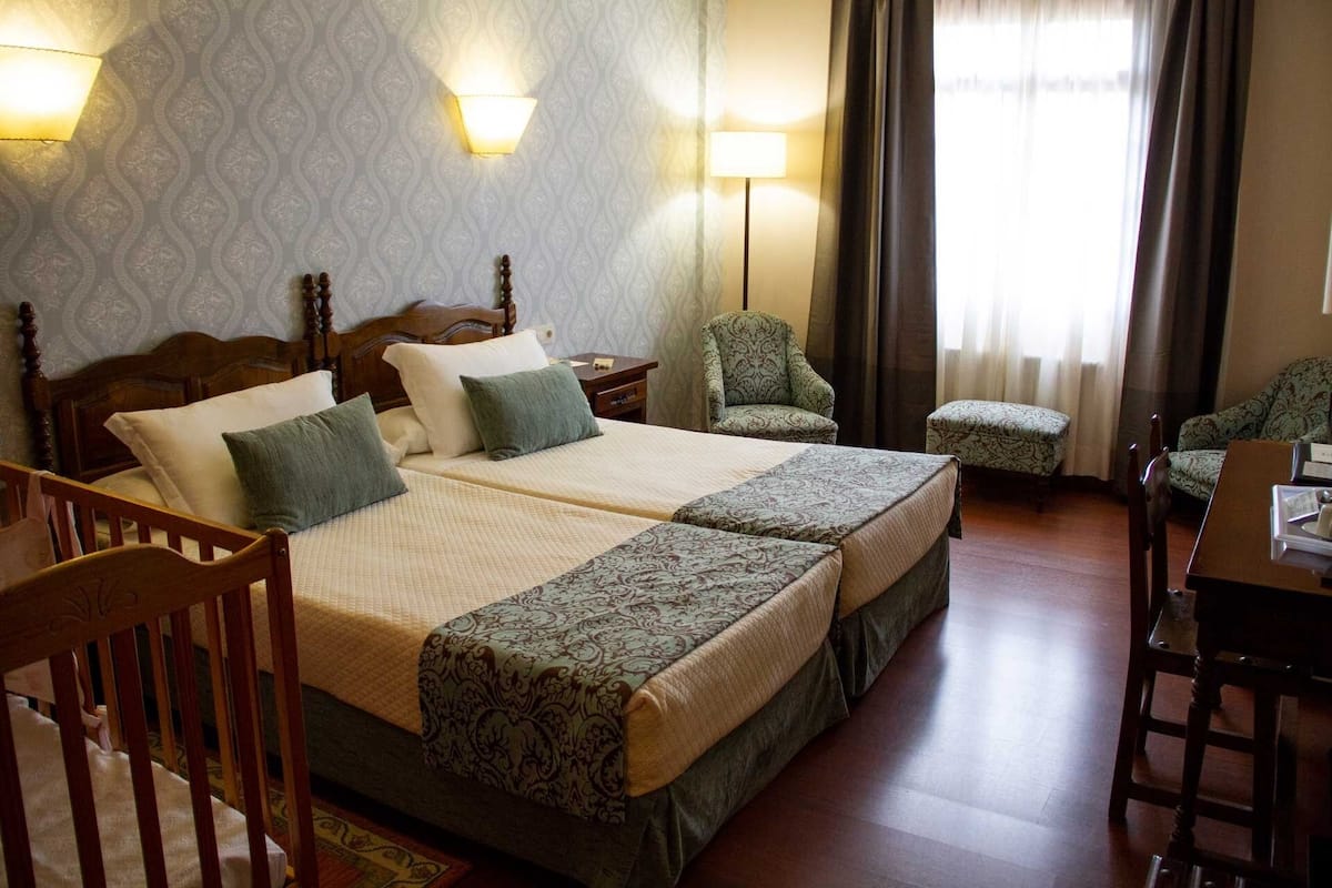 A hotel room with two beds, a chair, a desk, and a window with curtains.