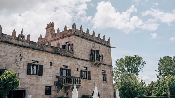 Un edificio histórico de piedra con múltiples ventanas y balcones, rodeado de follaje.