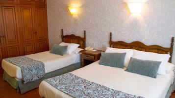 A hotel room with two single beds, wooden headboards, a nightstand with a telephone, and wall-mounted lights.