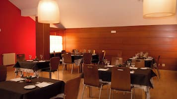 A dining area with multiple tables set for a meal, chairs, and hanging lamps.