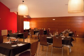A dining area with multiple tables set for a meal, chairs, and hanging lamps.