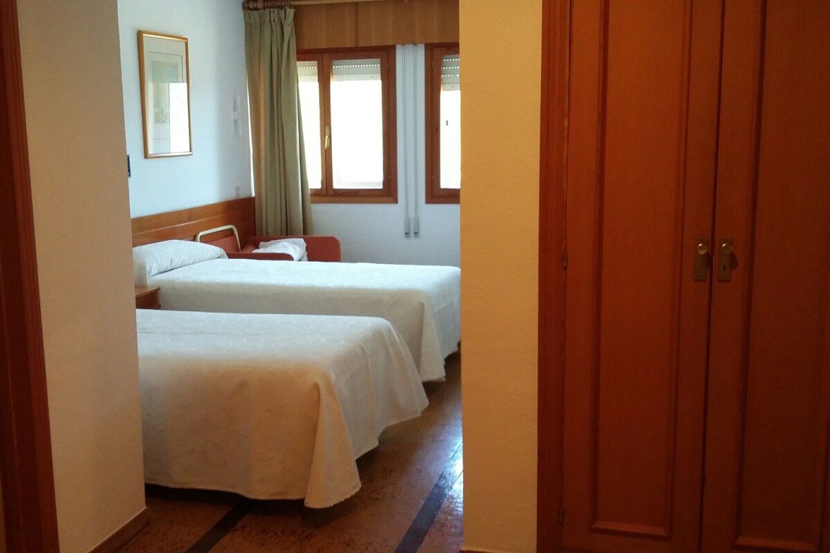 Habitación de hotel con dos camas, una puerta de madera y una ventana con cortinas.