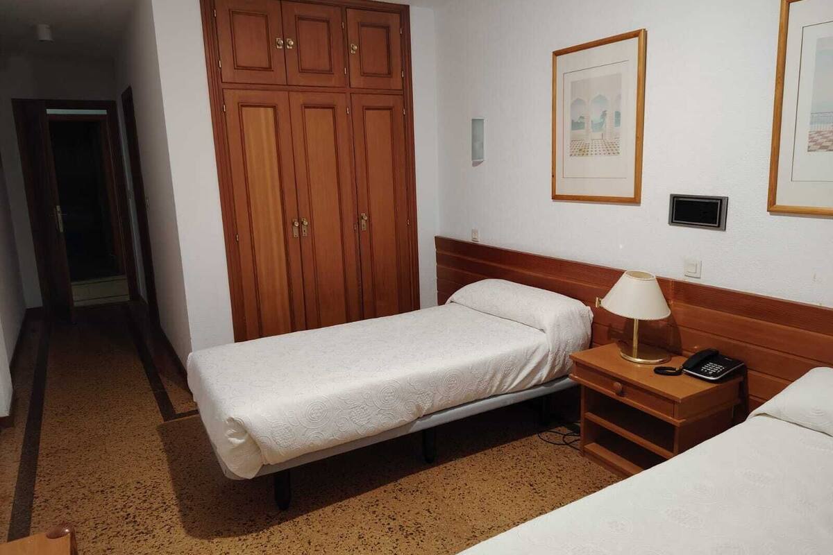 Una habitación de hotel con una cama individual, una mesita de noche con lámpara, un teléfono y un armario.