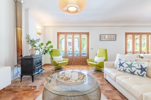 Un salon avec une cheminée, des fauteuils verts, un canapé blanc et une table basse en verre.