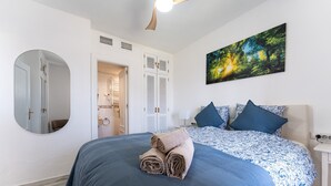A bedroom with a bed, a mirror, a door, a painting, and a nightstand.