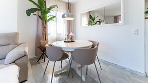 A modern dining area with a round table, four chairs, a hanging light fixture, a large potted plant, a mirror, and a sofa.