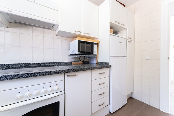 Cucina con mobili bianchi, forno a microonde, piano cottura e frigorifero.