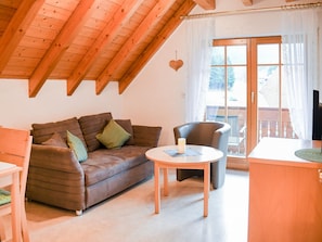 Ein gemütlicher Raum mit Holzbalkendecke, einem braunen Sofa mit Kissen, einem kleinen runden Tisch und einem Sessel.