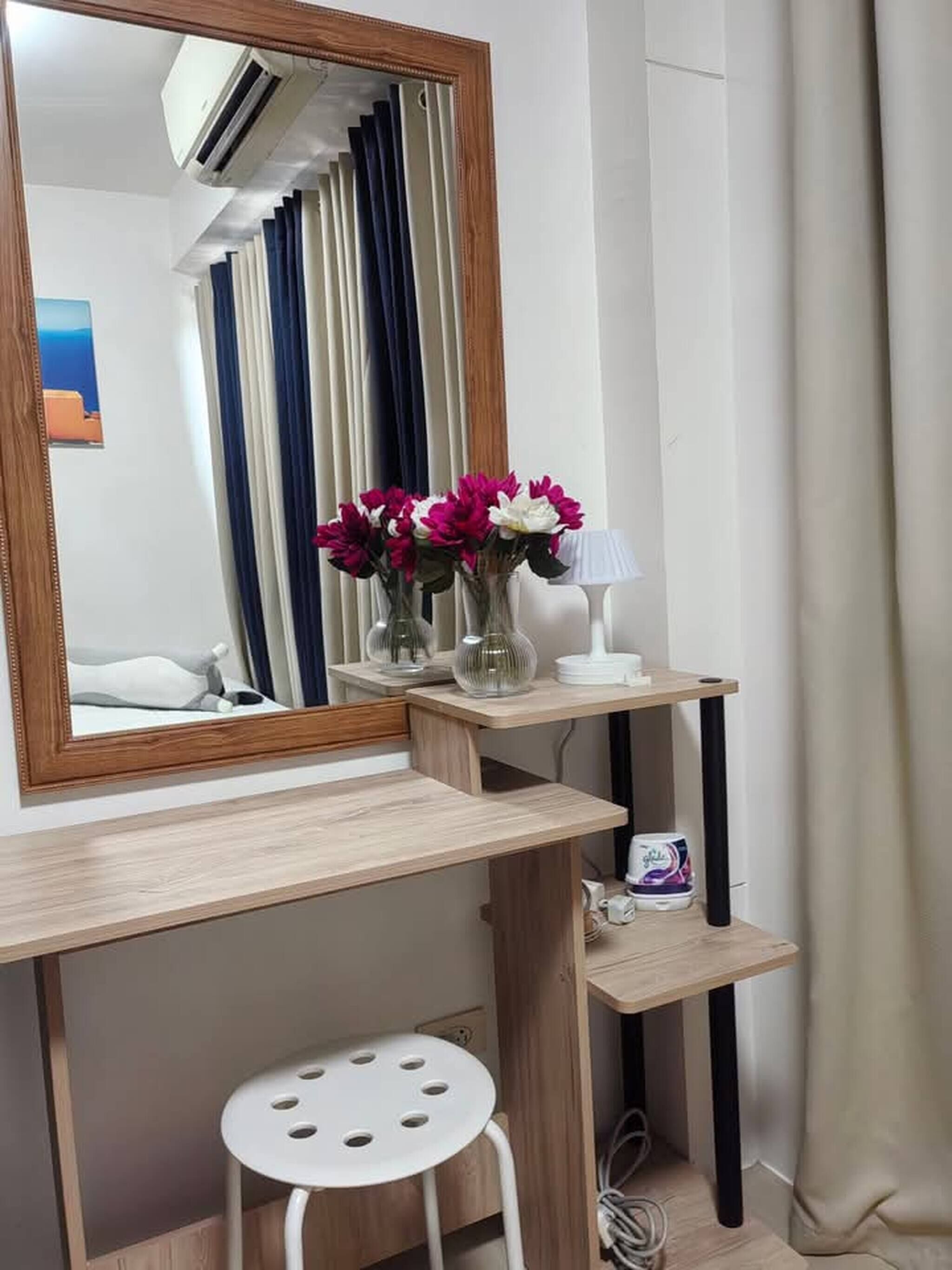 Une pièce comprenant une coiffeuse en bois, un miroir, un tabouret, une lampe et un vase avec des fleurs.