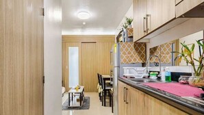 A modern kitchen with wooden cabinets, a countertop, and a dining area with chairs and a table. - The Golden Shore Suites (Pasay)