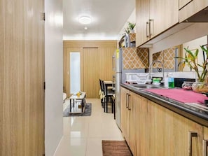 A modern kitchen with wooden cabinets, a countertop, and a dining area with chairs and a table. - The Golden Shore Suites (Pasay)