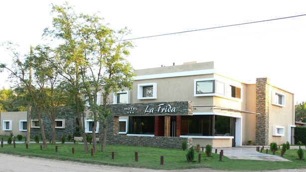 Ein modernes Hotel namens "La Frida" mit einer Steinfassade, zahlreichen Fenstern und einem gepflegten Rasen.