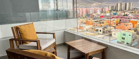 Un balcón con una silla y mesa de madera, que ofrece vistas a edificios coloridos y montañas.