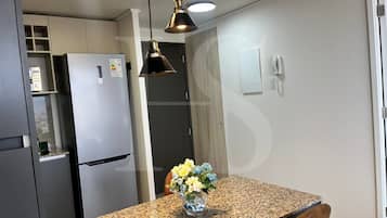 Cozinha com geladeira de aço inoxidável, forno embutido, bancada de granito, luminária pendente e telefone fixado na parede.
