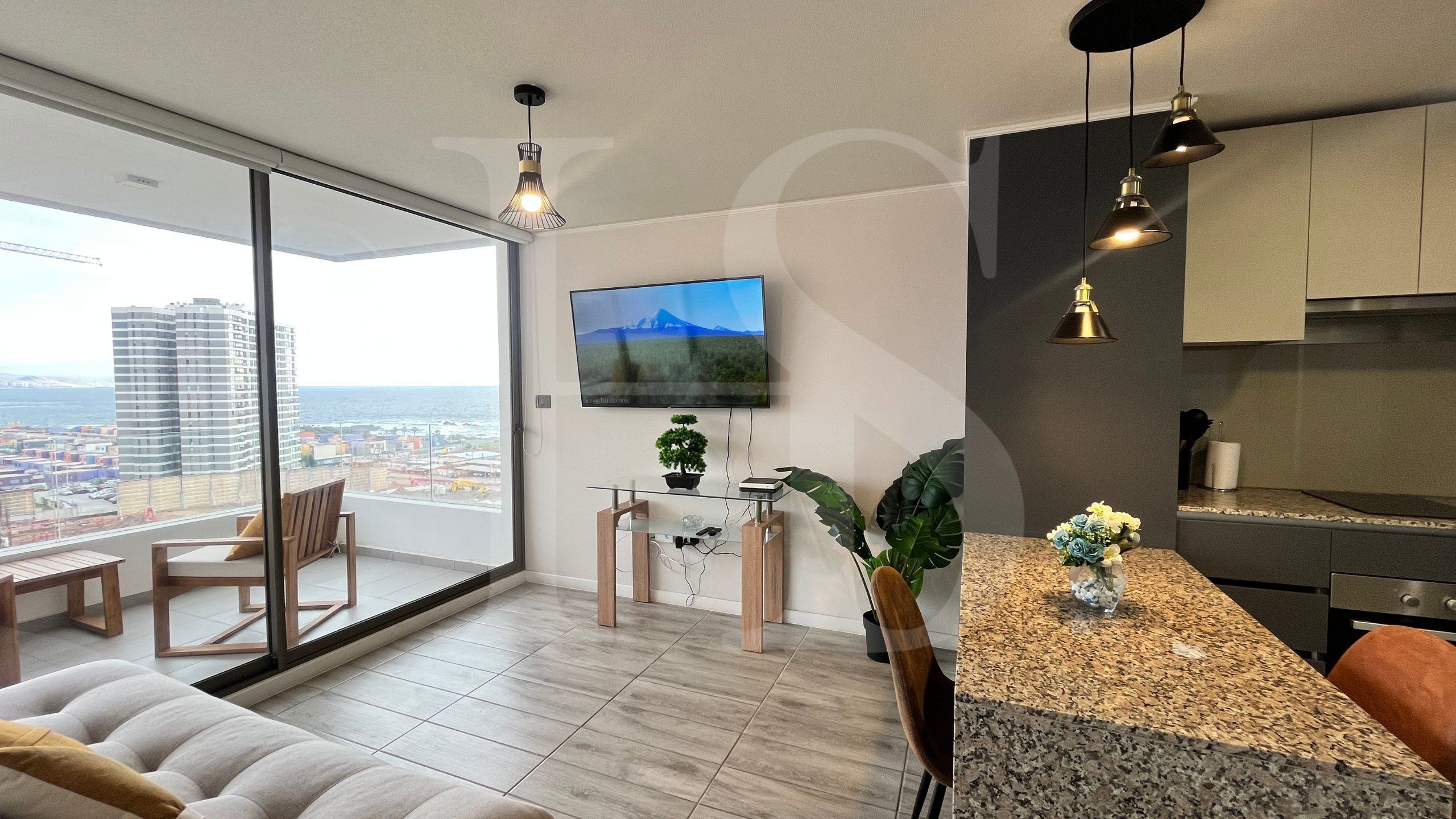 A modern apartment with a balcony, a flat-screen TV, a dining area, and a kitchen.