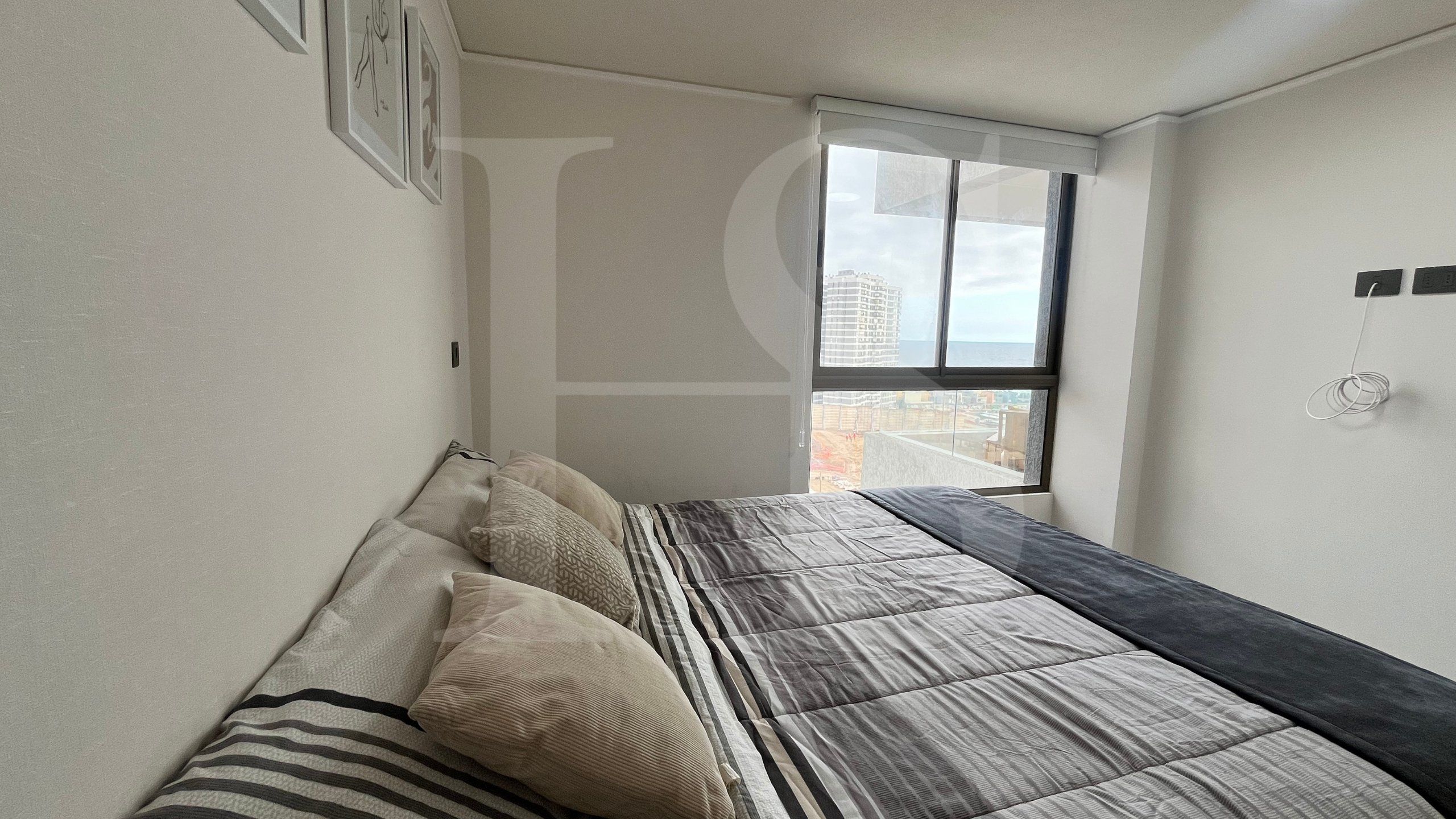 Un dormitorio con cama, almohadas, una ventana y vistas a edificios.