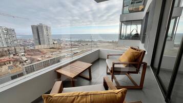 Balcón con vista al océano y una obra en construcción, amueblado con una silla y una mesa.