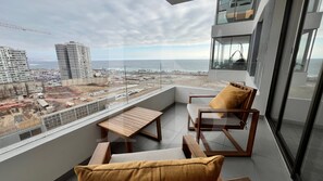 Balcón con vista al océano y una obra en construcción, amueblado con una silla y una mesa.