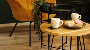 A room with a yellow chair, a round wooden table with a tray of pastries, and a view through a glass door. - 🏡 Detached chalet on the edge of the Veluwe - luxury, sauna, peace & space (Putten)