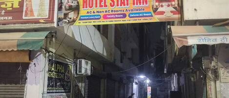 A hotel sign advertising AC and Non AC rooms, a 24-hour service, and a location near major transport hubs.