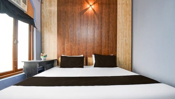 A bedroom with a large bed, wooden panel wall, and a nightstand with a lamp. - HOTEL STAY INN (Lucknow)