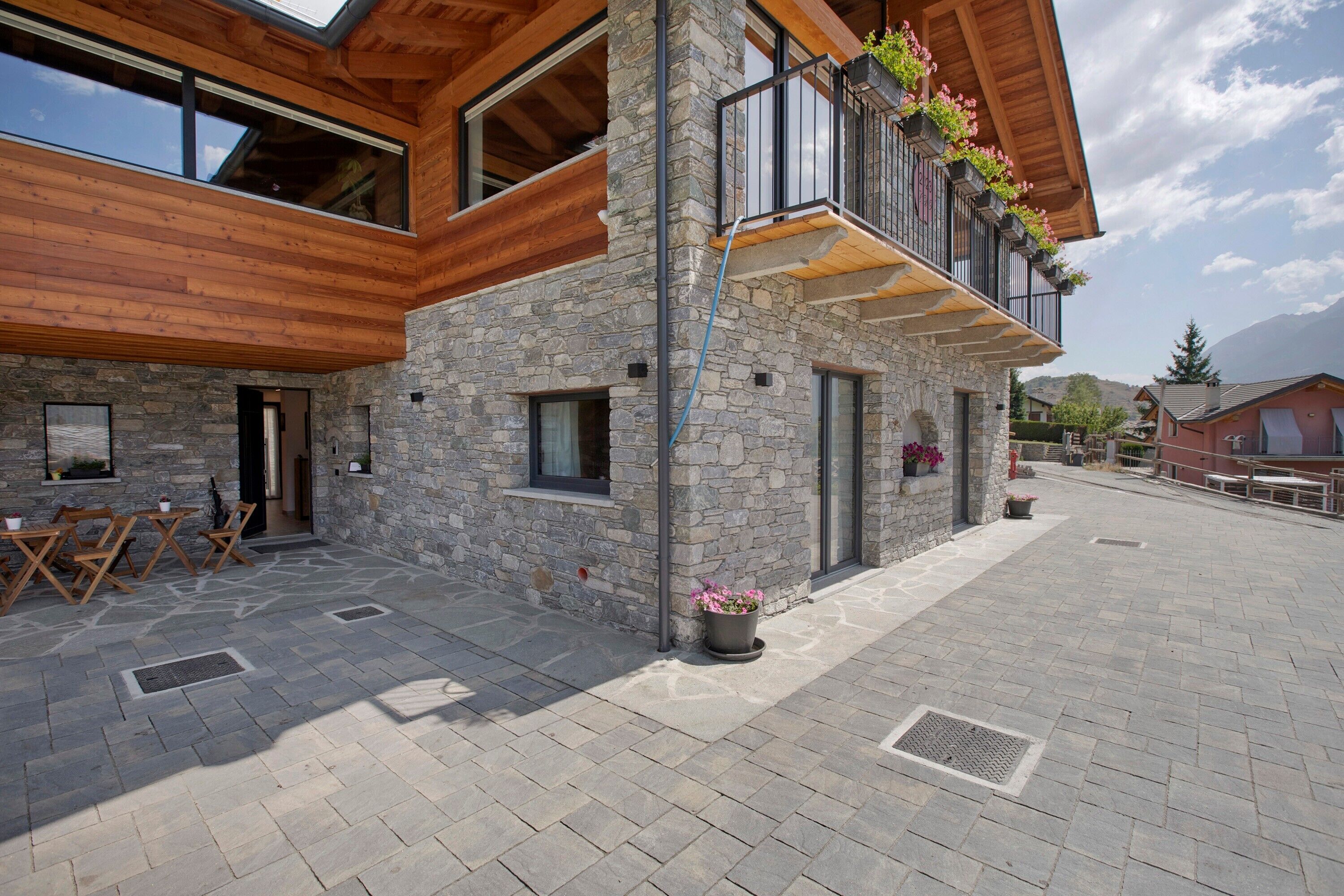 Un bâtiment en pierre avec un étage supérieur en bois, des places assises à l’extérieur et un balcon agrémenté de fleurs.