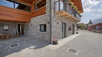 Un bâtiment en pierre avec un étage supérieur en bois, des places assises à l’extérieur et un balcon agrémenté de fleurs.