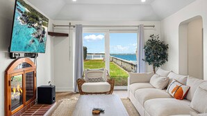 A living room with a fireplace, a television, a sofa, and a view of the ocean. - Blue Water (Southampton Parish)