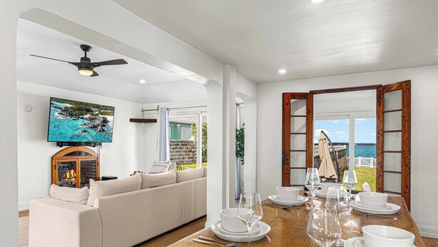 A dining area with a wooden table set for a meal, a sofa, and a TV displaying a scenic view. - Blue Water (Southampton Parish)