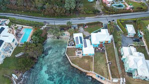 An aerial view of a coastal property with a swimming pool, multiple houses, and a dock extending into the water. - Blue Water (Southampton Parish)