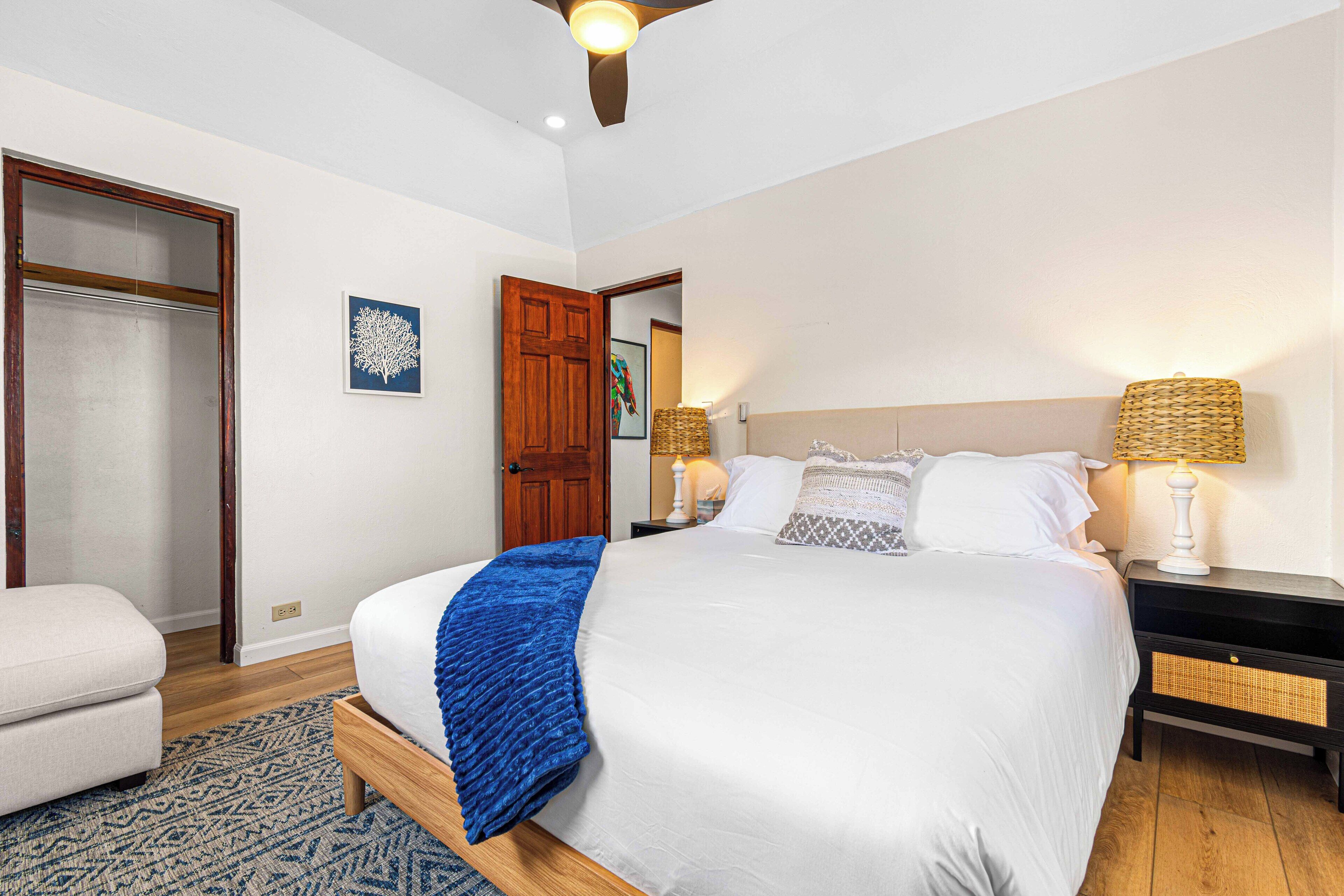 Quarto com cama, mesas de cabeceira, um banquinho e uma porta.